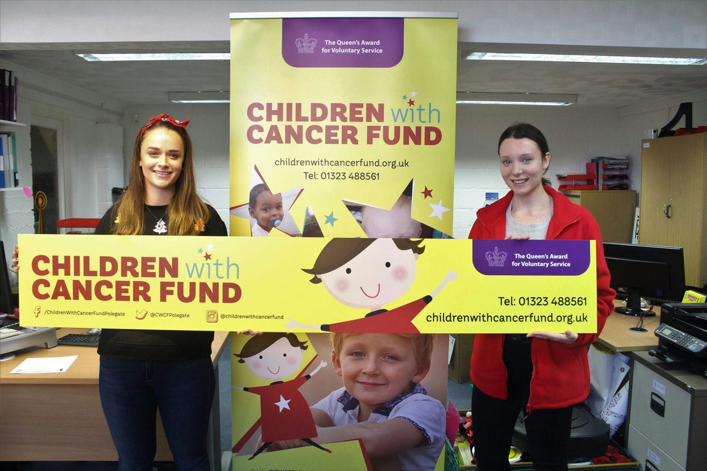 Two members of Identity hold up a sign saying children with cancer fund