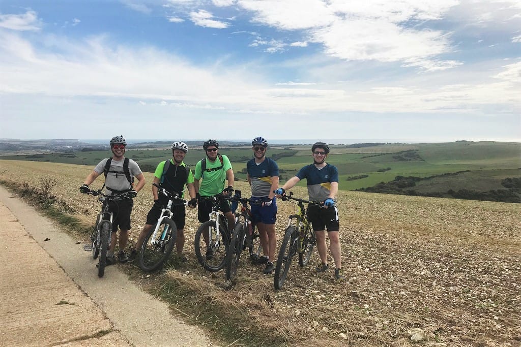 Five members of the Identity team with their bikes in front of a backdrop of green land