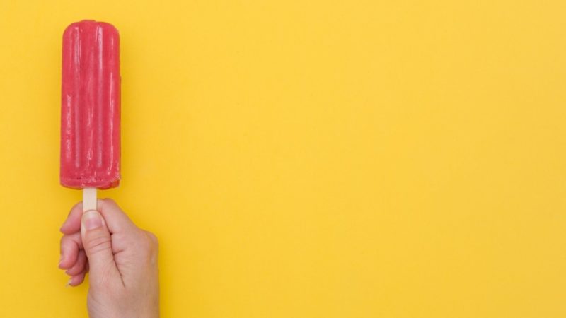 Hand holding an ice lolly against a yellow background